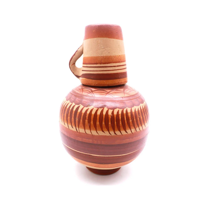 A handcrafted ceramic pitcher with a rounded body, a small handle, and a conical lid, decorated with terracotta, brown, and beige stripes and geometric patterns, set against a plain white background.