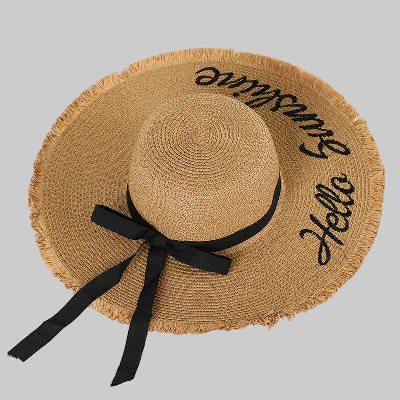 Brown straw hat with black ribbon and 'Bonjour Hello' text on a light background